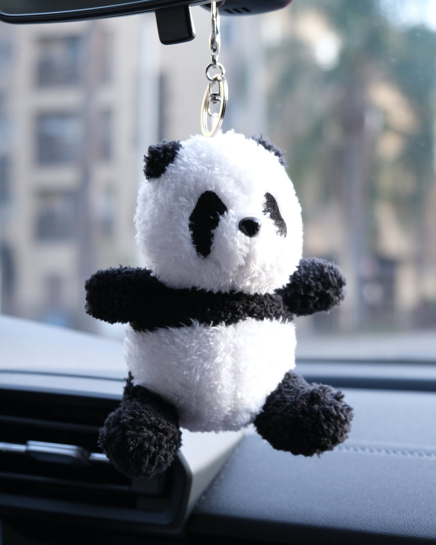 Panda plush keychain hanging from a car's rearview mirror with a blurred outdoor background.