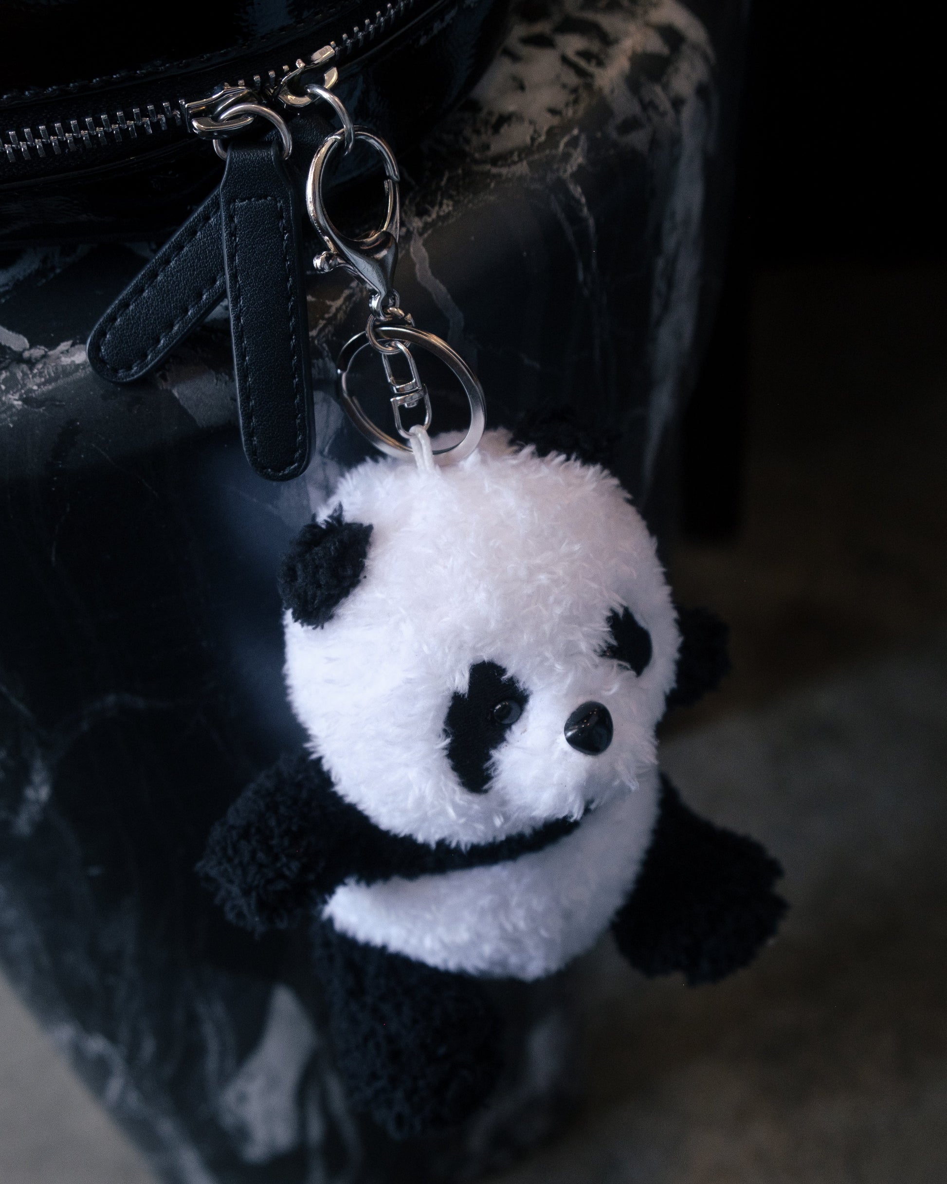 Cute panda plush keychain hanging from a backpack zipper, adding a soft and adorable accessory to everyday bags.
