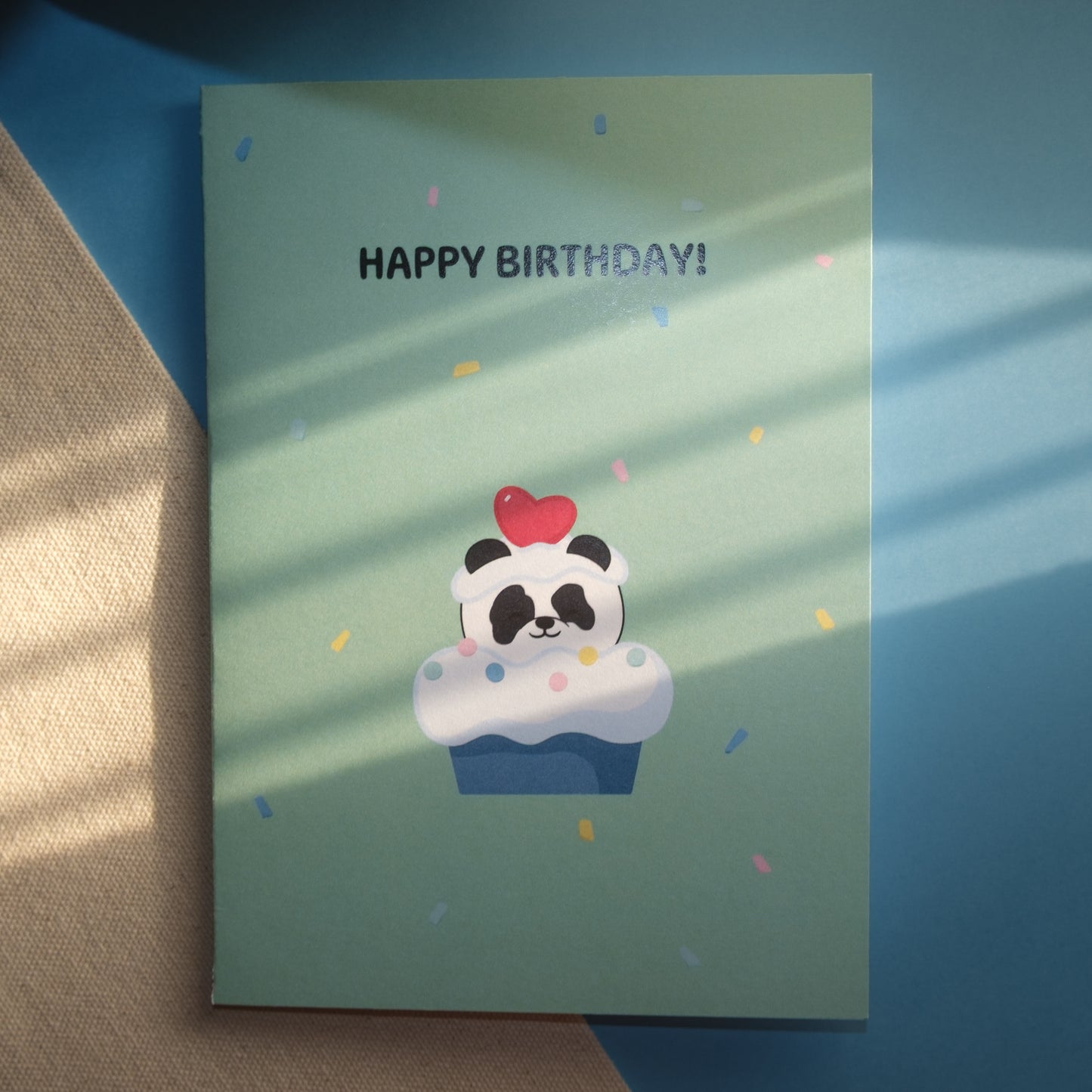 Light green greeting card with a cute panda popping out of a cupcake with a heart of his head and confetti ,and the text, "HAPPY BIRTHDAY!"