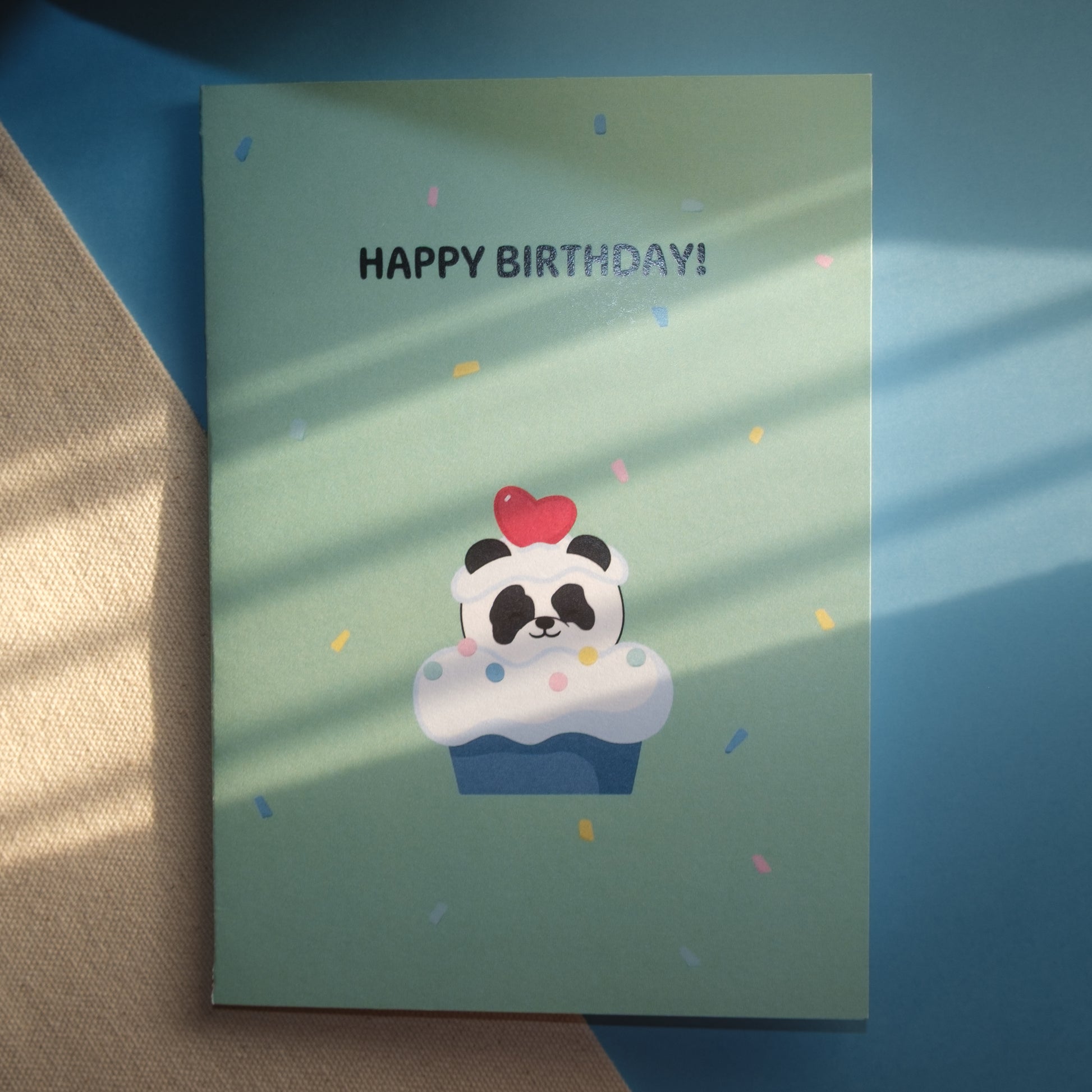 Light green greeting card with a cute panda popping out of a cupcake with a heart of his head and confetti ,and the text, "HAPPY BIRTHDAY!"