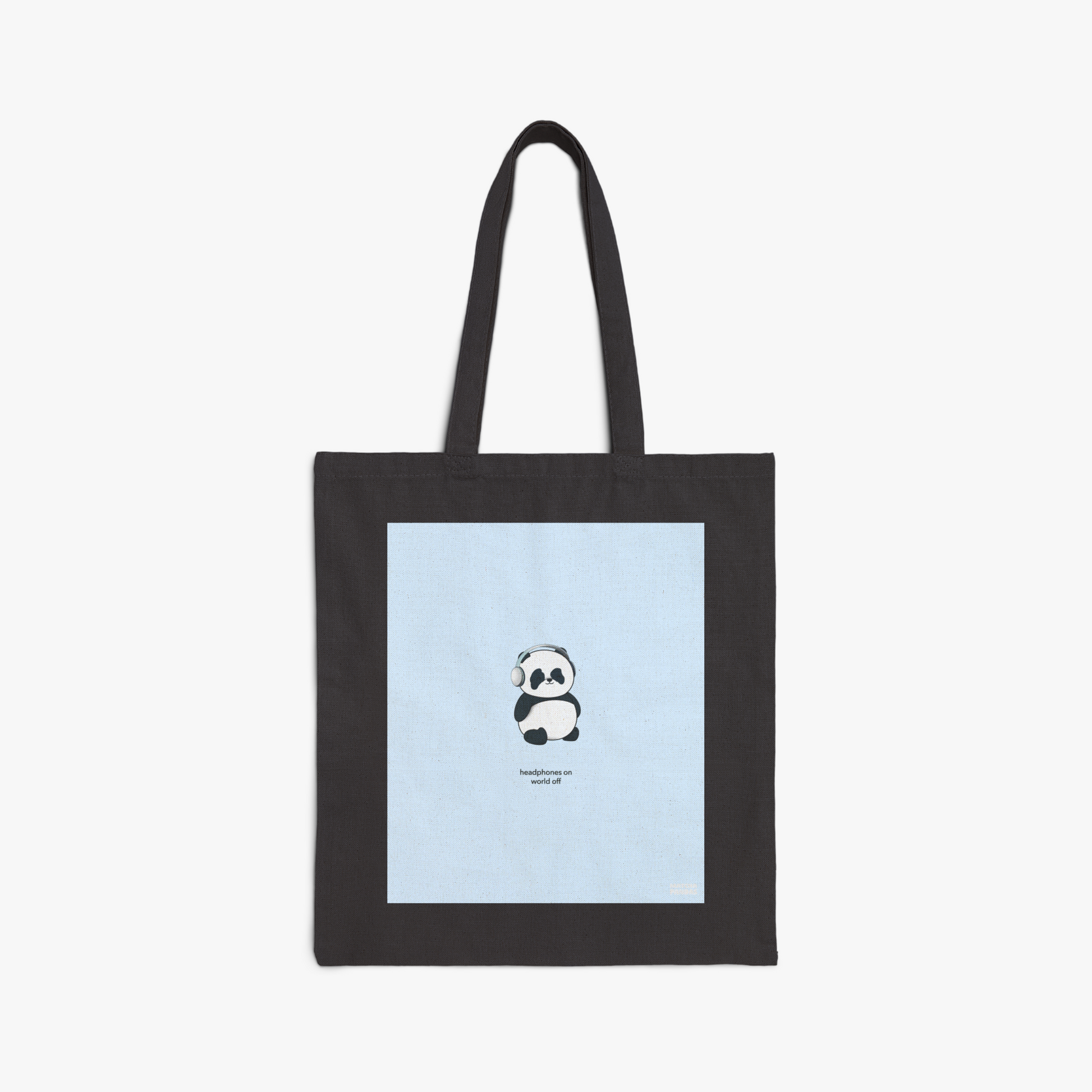 Black tote bag with large graphic print of our panda wearing headphones with the phrase, "headphones on world off," on blue background 