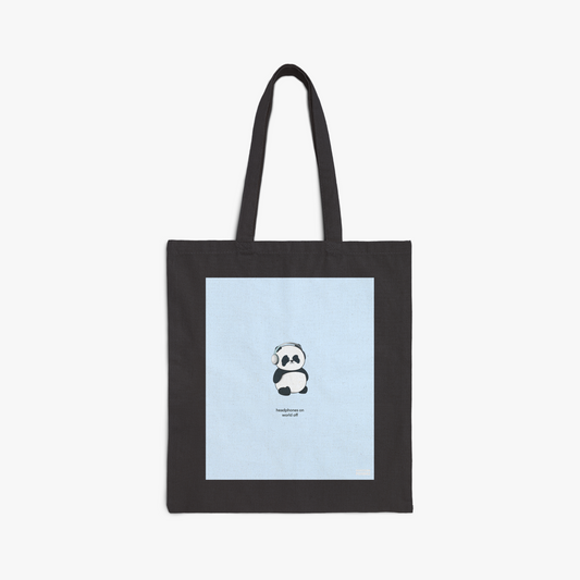 Black tote bag with large graphic print of our panda wearing headphones with the phrase, "headphones on world off," on blue background 