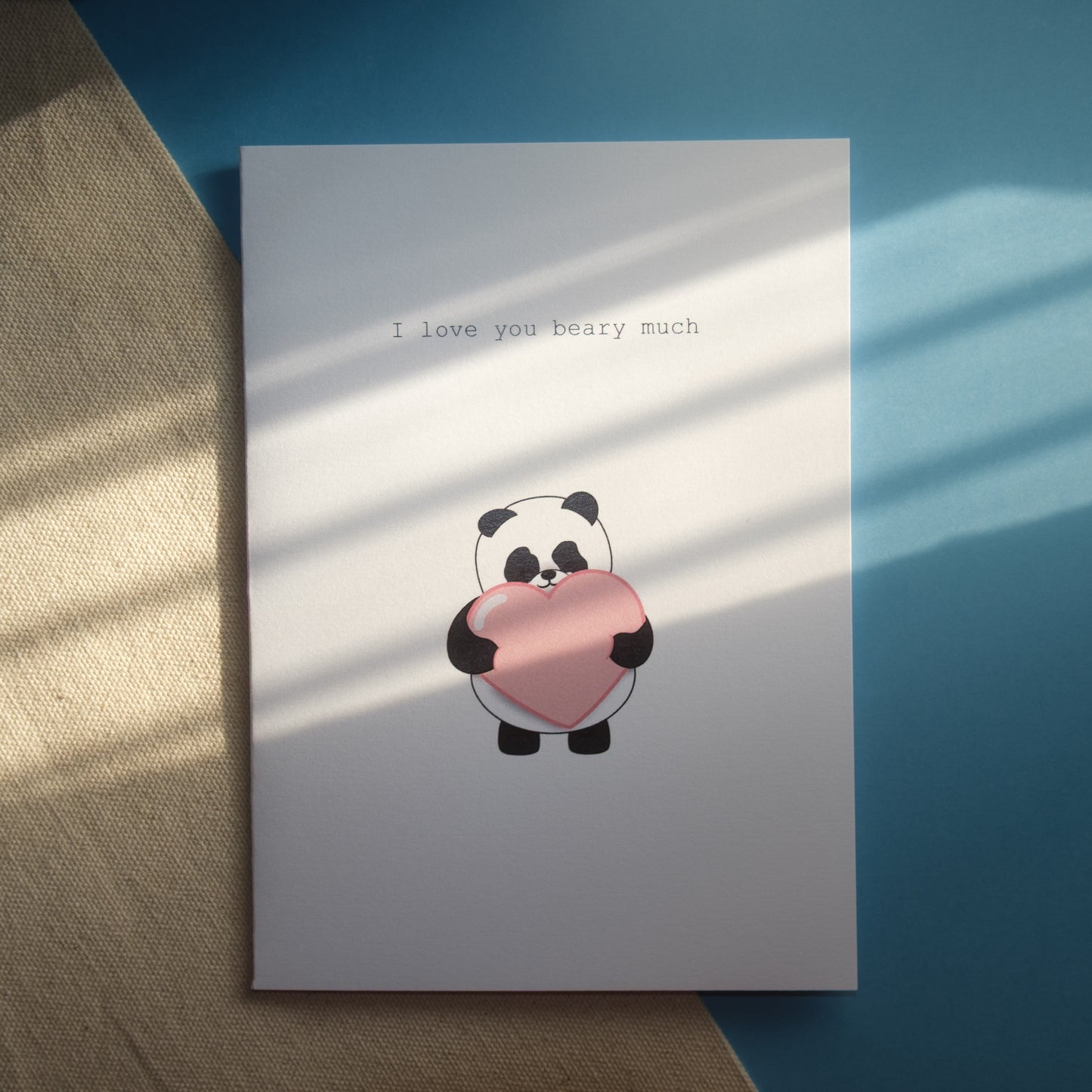 White greeting card of our panda holding a large pink heart with the text, "I love you beary much."