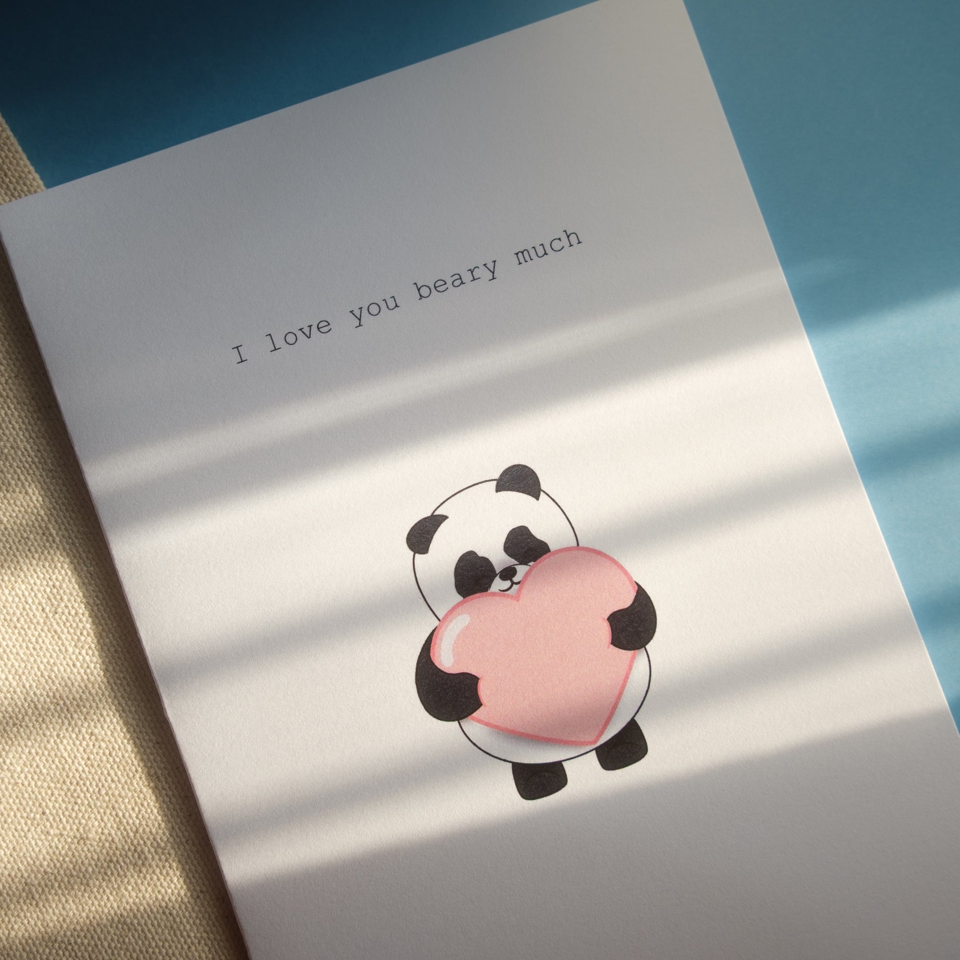 Close-up of White greeting card of our panda holding a large pink heart with the text, "I love you beary much"
