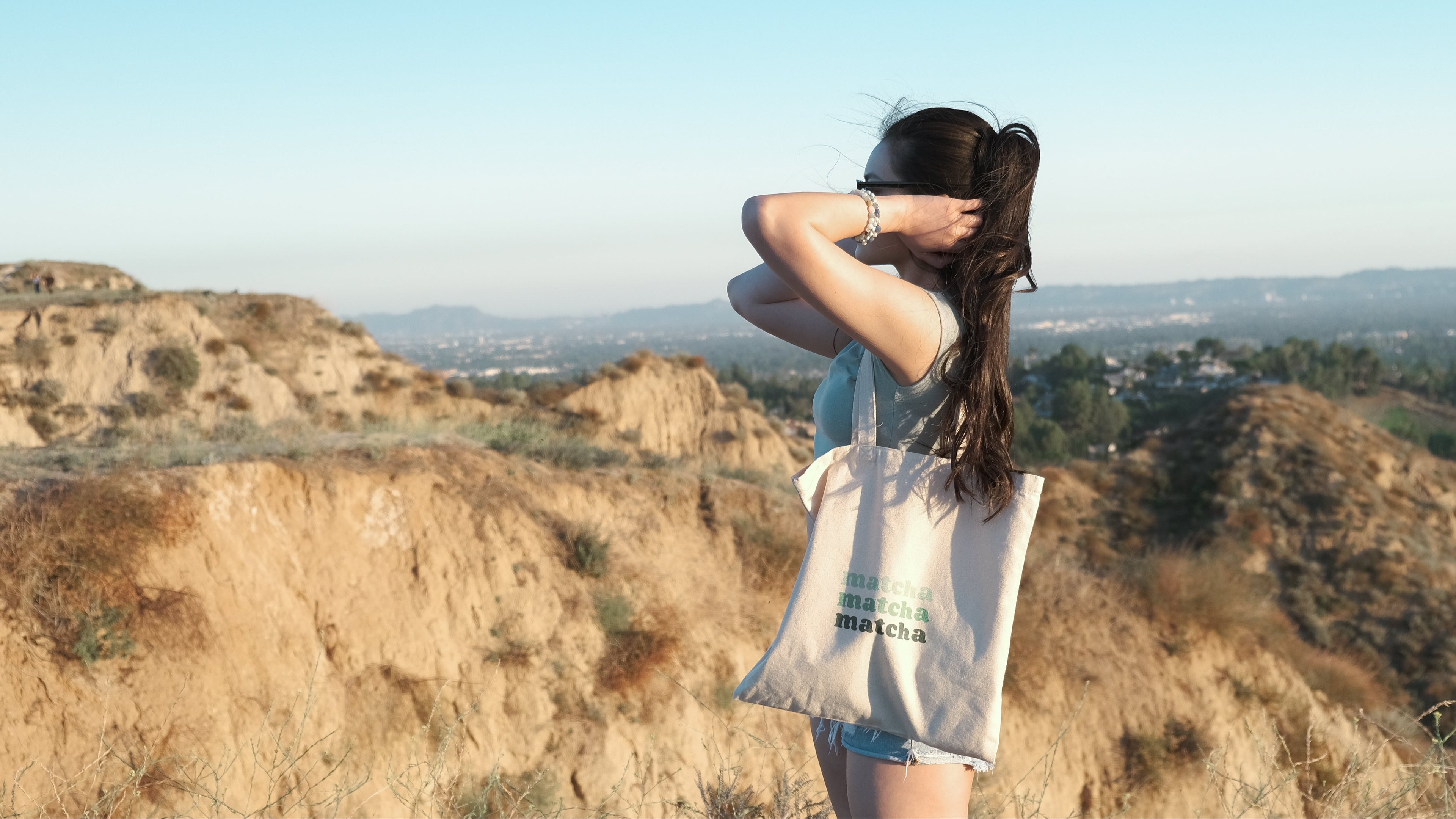 Model wears canvas tote bag with text, "matcha matcha matcha" in green gradient. 