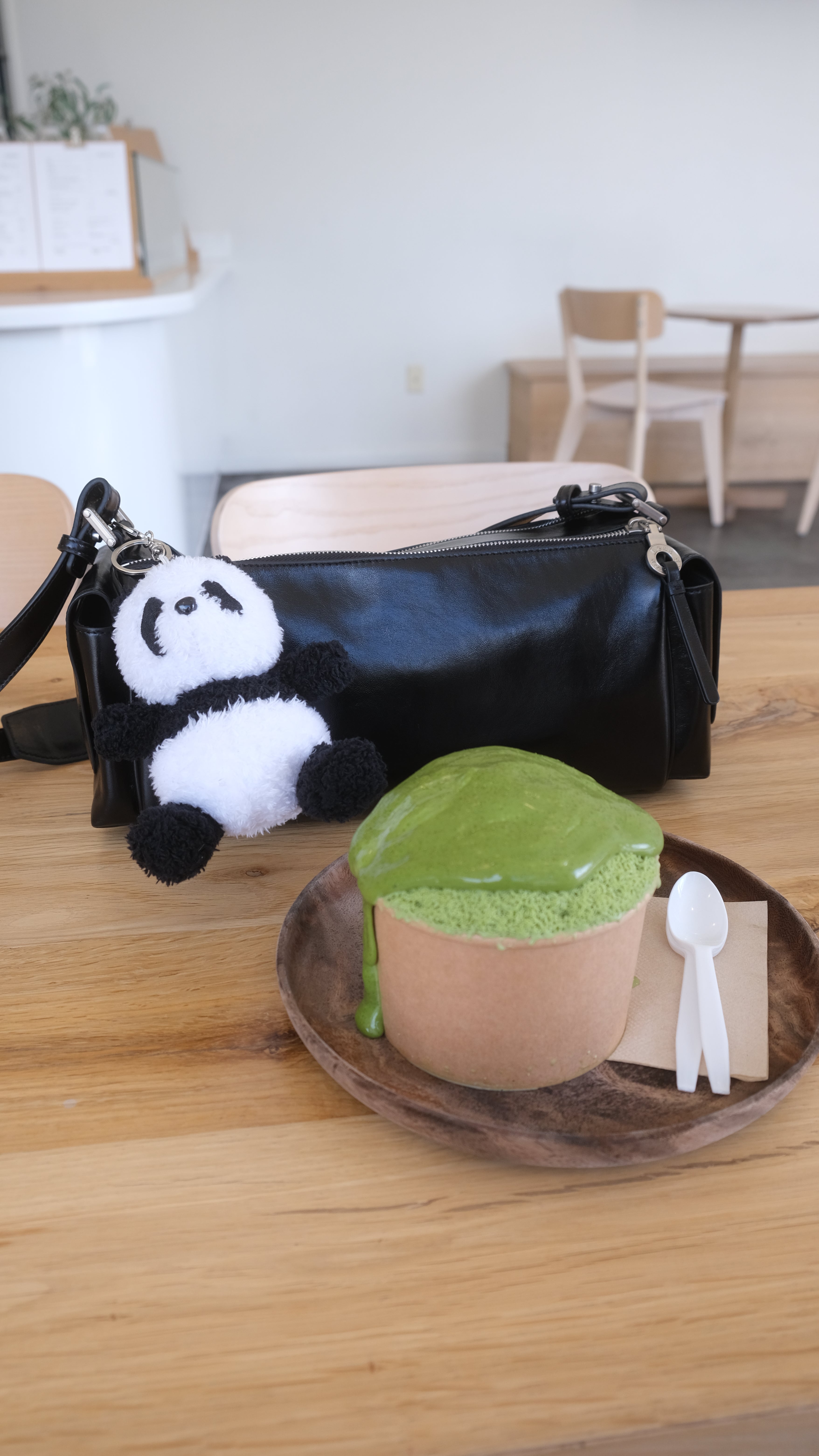 Our panda plush keychain hangs off a black handbag that rests on top of a table that shares a matcha shave ice treat.