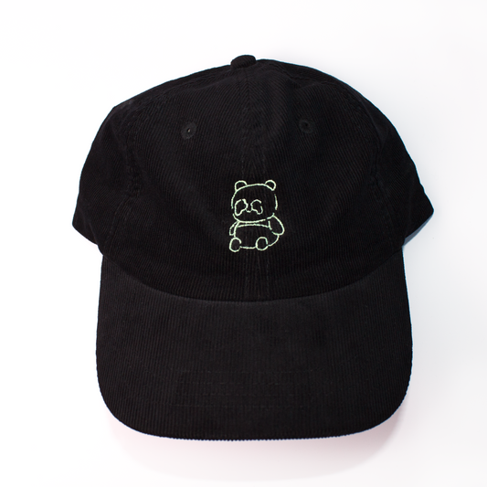 A black baseball cap made of textured corduroy fabric, featuring a small green embroidered panda bear on the front, set against a plain white background.