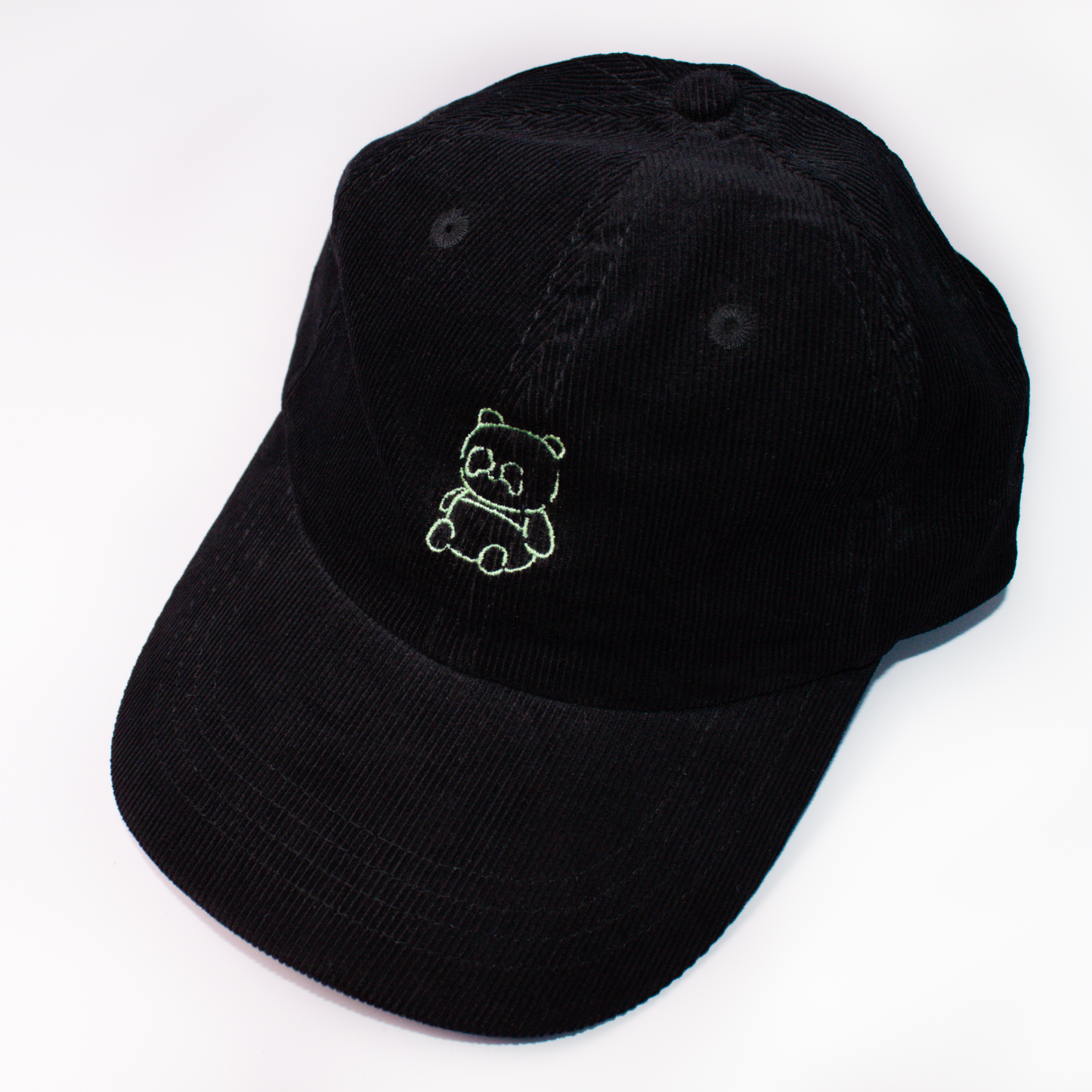 A black corduroy baseball cap featuring a small green embroidered panda bear on the front, set against a plain white background.