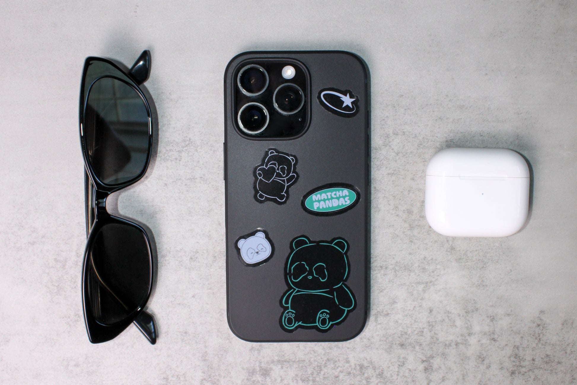 Phone case with stickers, sunglasses, and AirPods on a gray surface