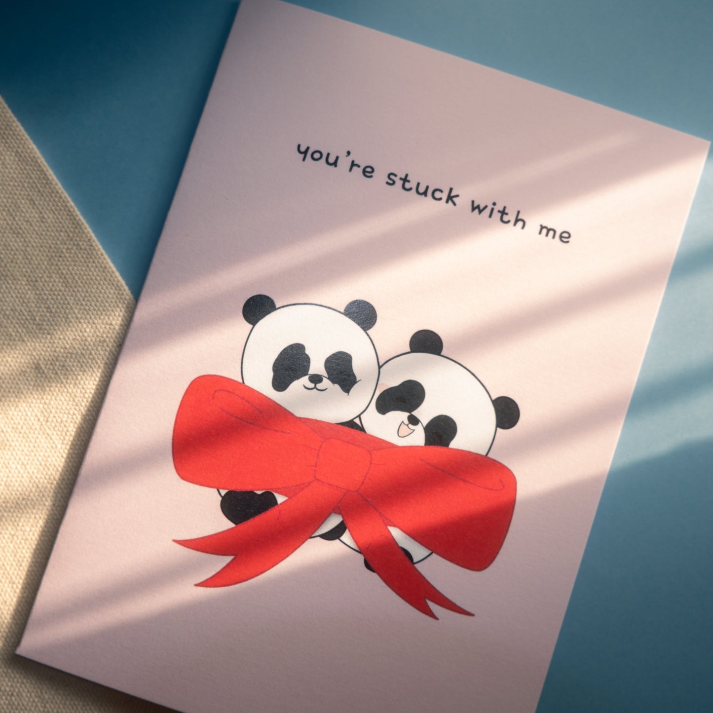 Pink card with two pandas wrapped in a large red bow with the text "you're stuck with me." 