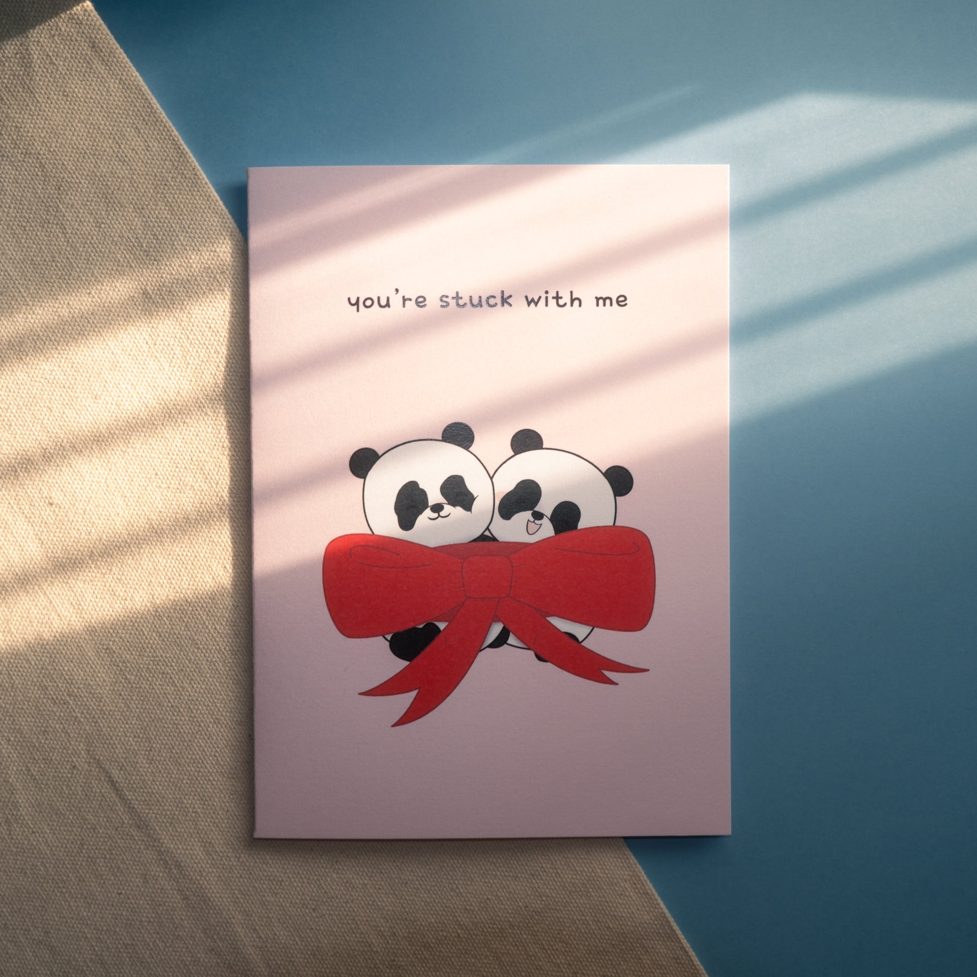 Pink card of 2 pandas wrapped inside a large red bow with the text, "you're stuck with me"